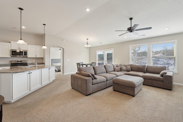 living room featuring light colored carpet, lofted ceiling, and ceiling fan with notable chandelier