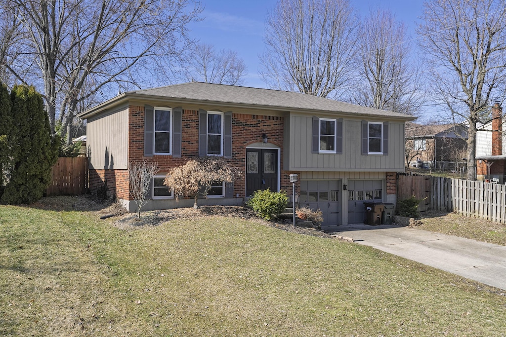 split foyer home with a garage, brick siding, a front yard, and fence