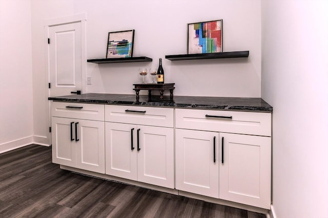 bar featuring dark hardwood / wood-style floors, dark stone countertops, and white cabinetry