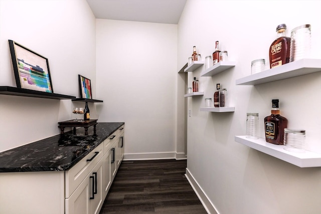 bar with dark wood-type flooring, white cabinetry, and dark stone countertops