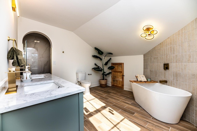 bathroom with vanity, tile walls, toilet, a tub to relax in, and vaulted ceiling