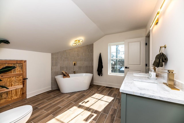 bathroom with toilet, vanity, vaulted ceiling, tile walls, and a tub to relax in