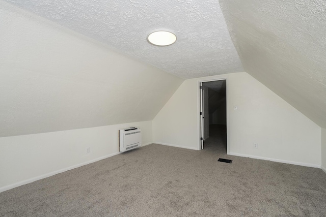 bonus room featuring a textured ceiling, carpet, heating unit, and vaulted ceiling