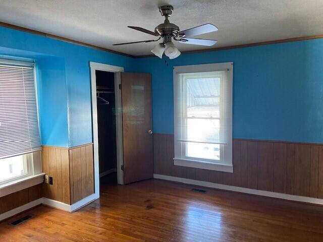 unfurnished bedroom with ceiling fan, a closet, hardwood / wood-style floors, and multiple windows