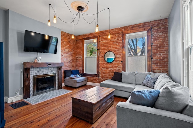 living room featuring wood-type flooring, a fireplace, brick wall, and a notable chandelier