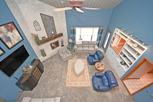 living room featuring ceiling fan, a tile fireplace, a towering ceiling, and carpet flooring