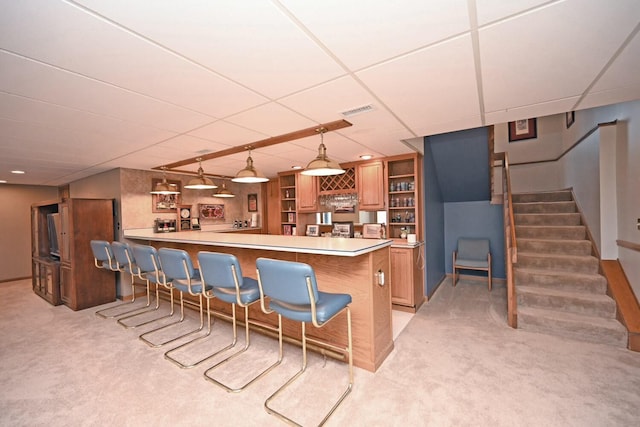 kitchen with pendant lighting, a drop ceiling, a kitchen bar, light carpet, and kitchen peninsula