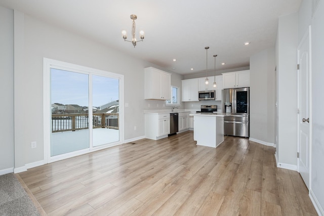 kitchen with appliances with stainless steel finishes, hanging light fixtures, a center island, light hardwood / wood-style floors, and white cabinets