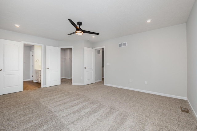 unfurnished bedroom with a walk in closet, ensuite bathroom, ceiling fan, and carpet flooring