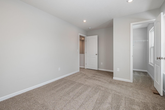 unfurnished bedroom featuring a spacious closet, light colored carpet, and a closet