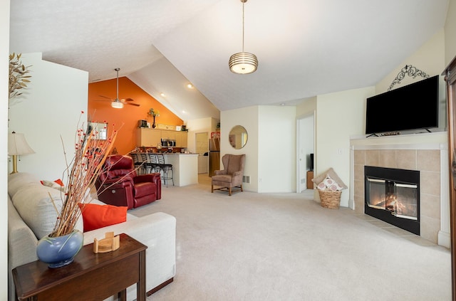 living room featuring vaulted ceiling, ceiling fan, light carpet, and a tiled fireplace