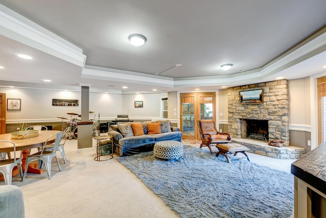 carpeted living room featuring a raised ceiling, crown molding, and a stone fireplace