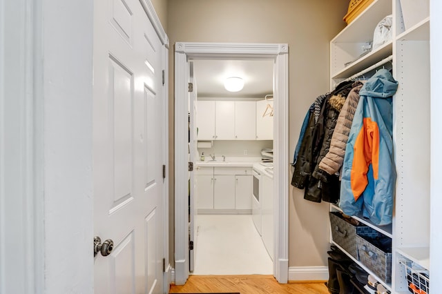 clothes washing area with cabinets, sink, washing machine and clothes dryer, and light hardwood / wood-style flooring