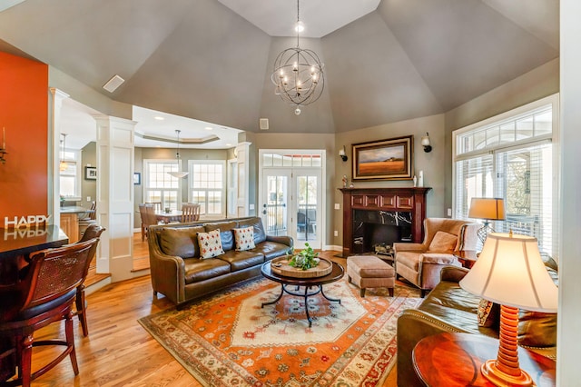 living room featuring ornate columns, high vaulted ceiling, a chandelier, a high end fireplace, and light hardwood / wood-style flooring