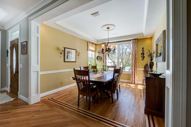 dining area featuring ornamental molding, a raised ceiling, hardwood / wood-style floors, and a notable chandelier