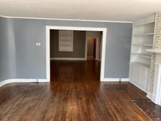 spare room with a brick fireplace, dark hardwood / wood-style flooring, and built in shelves