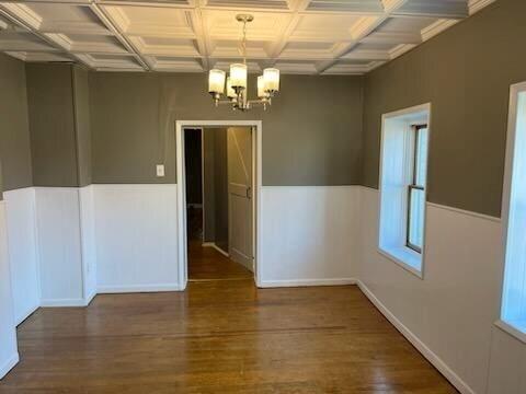 unfurnished room featuring coffered ceiling, a notable chandelier, beam ceiling, and dark hardwood / wood-style floors