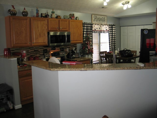 kitchen with vaulted ceiling, kitchen peninsula, appliances with stainless steel finishes, and decorative backsplash