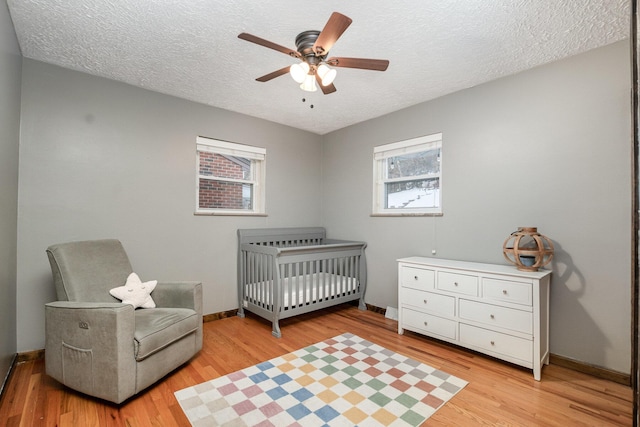 bedroom with a crib, a textured ceiling, ceiling fan, and light hardwood / wood-style floors