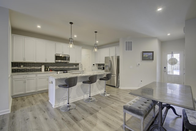 kitchen featuring decorative light fixtures, a center island with sink, white cabinets, and appliances with stainless steel finishes