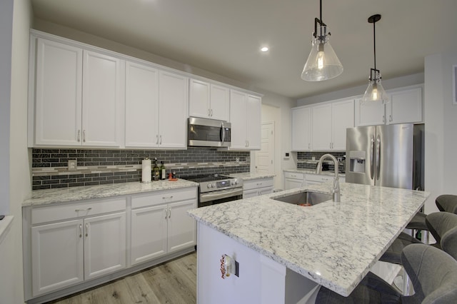 kitchen featuring sink, white cabinetry, hanging light fixtures, stainless steel appliances, and a center island with sink