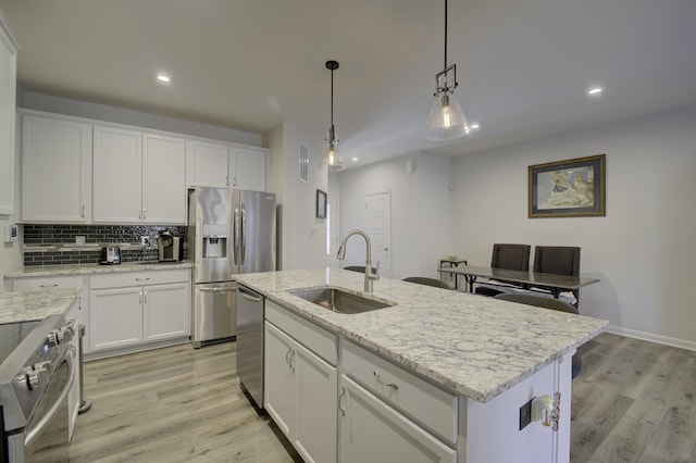 kitchen with appliances with stainless steel finishes, decorative light fixtures, an island with sink, sink, and white cabinets