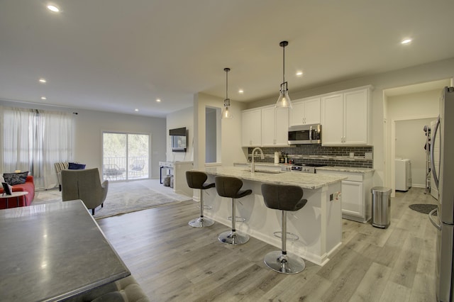 kitchen with appliances with stainless steel finishes, white cabinetry, light stone countertops, an island with sink, and decorative light fixtures