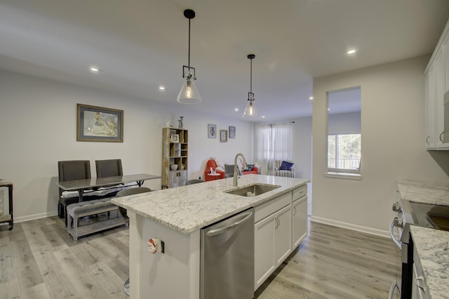 kitchen with sink, appliances with stainless steel finishes, light stone counters, white cabinets, and a center island with sink