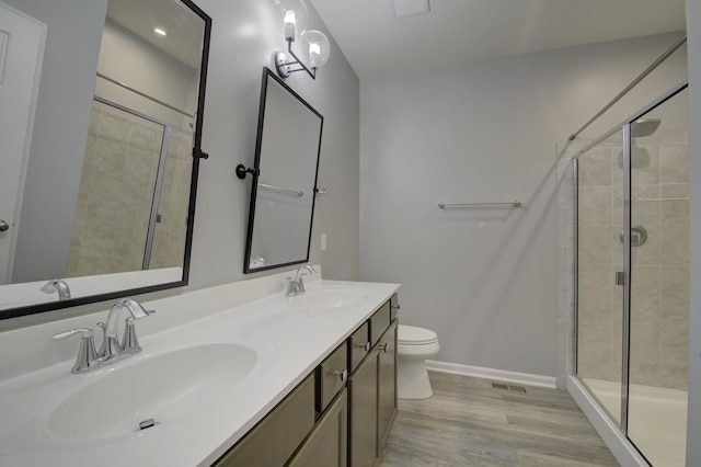 bathroom featuring wood-type flooring, toilet, a shower with shower door, and vanity