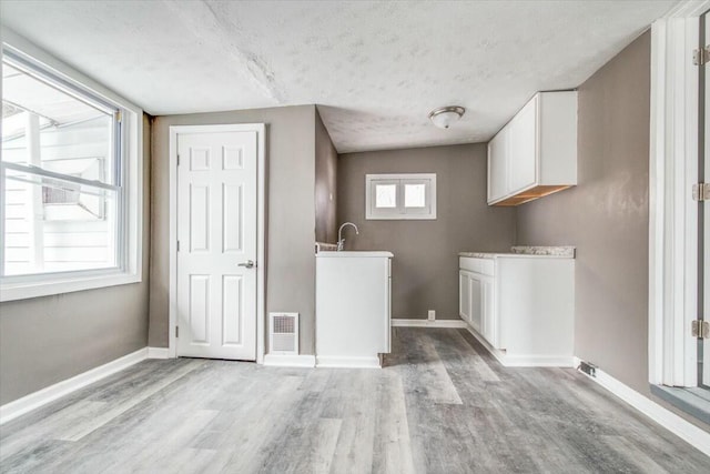 clothes washing area with sink, a textured ceiling, and light hardwood / wood-style flooring