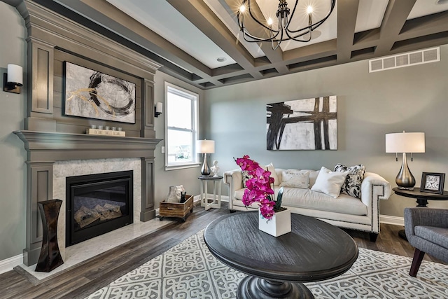 living room featuring dark wood-type flooring, beamed ceiling, a large fireplace, a chandelier, and coffered ceiling