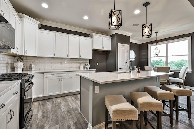 kitchen with hanging light fixtures, sink, white cabinetry, black gas range, and a center island with sink