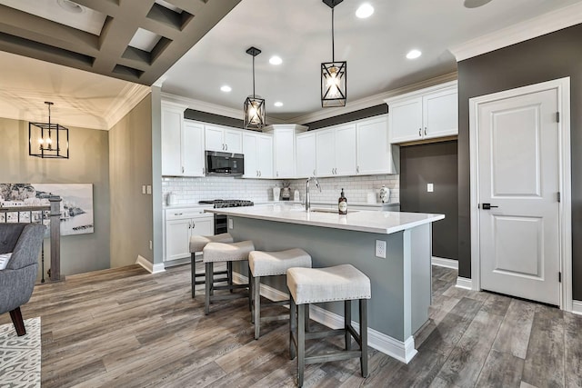 kitchen featuring white cabinets, appliances with stainless steel finishes, decorative light fixtures, a center island with sink, and coffered ceiling