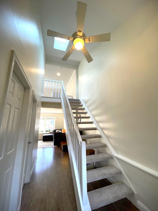 stairway with ceiling fan, a towering ceiling, wood-type flooring, and a skylight