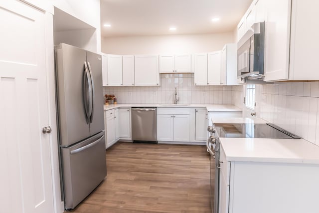 kitchen with appliances with stainless steel finishes, sink, white cabinets, decorative backsplash, and light wood-type flooring