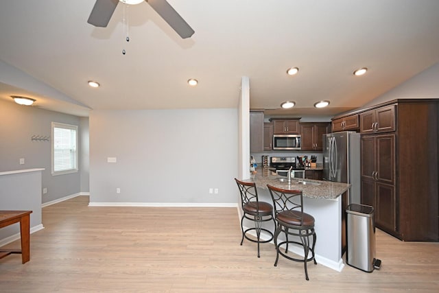 kitchen featuring sink, light stone counters, vaulted ceiling, dark brown cabinets, and appliances with stainless steel finishes