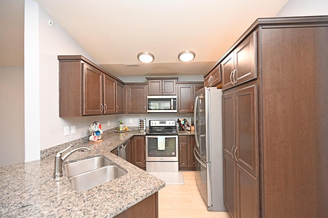 kitchen featuring sink, light wood-type flooring, appliances with stainless steel finishes, kitchen peninsula, and light stone countertops