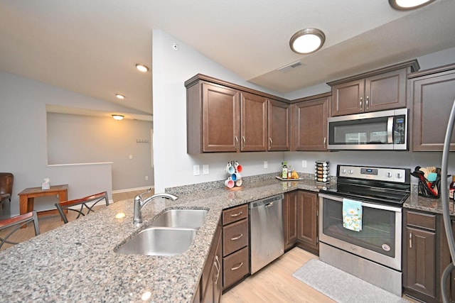 kitchen with sink, stainless steel appliances, light stone countertops, vaulted ceiling, and light wood-type flooring