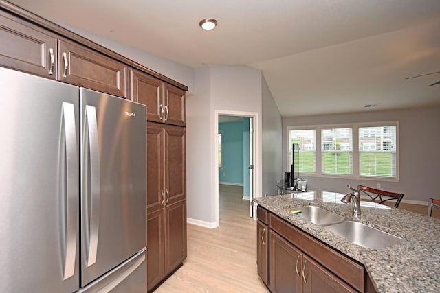 kitchen with lofted ceiling, sink, stainless steel fridge, and light stone countertops