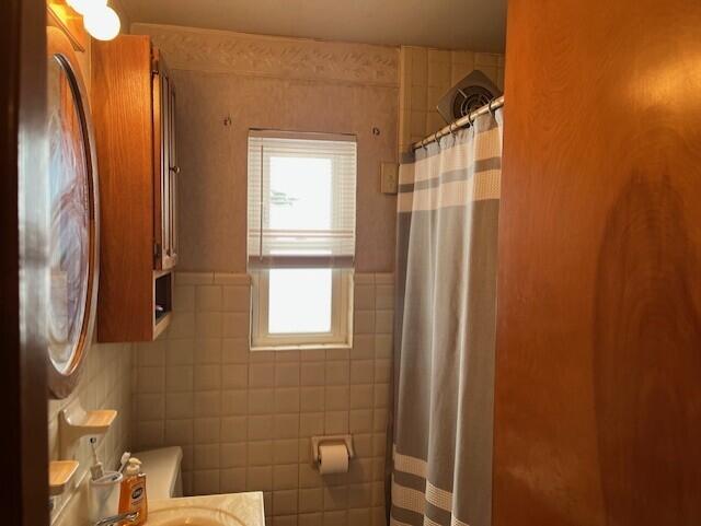 bathroom featuring toilet, curtained shower, and tile walls