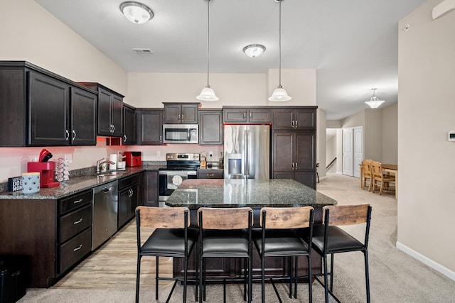 kitchen with a kitchen island, appliances with stainless steel finishes, dark stone counters, hanging light fixtures, and light carpet