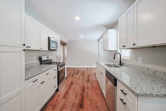 kitchen featuring sink, hardwood / wood-style flooring, white cabinetry, stainless steel appliances, and light stone countertops