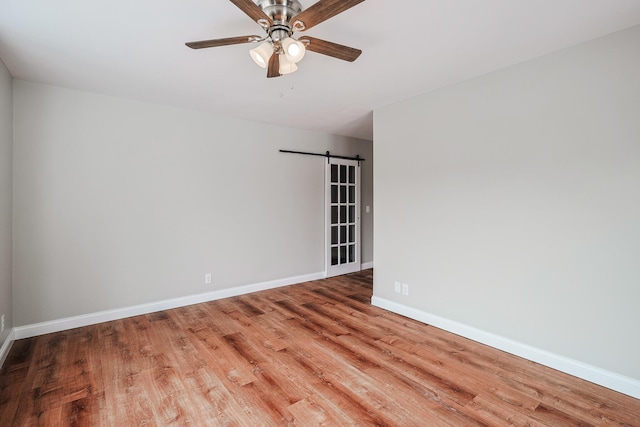 spare room with hardwood / wood-style flooring, ceiling fan, and a barn door