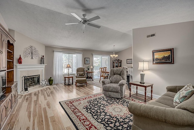 living room featuring light hardwood / wood-style flooring, ceiling fan with notable chandelier, vaulted ceiling, and a textured ceiling