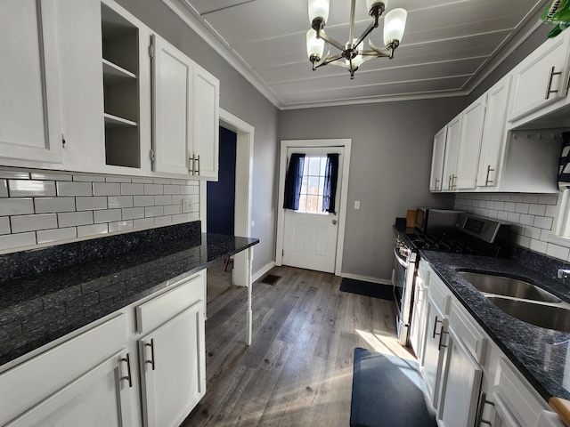 kitchen featuring stainless steel gas stove, crown molding, decorative light fixtures, dark stone countertops, and white cabinets