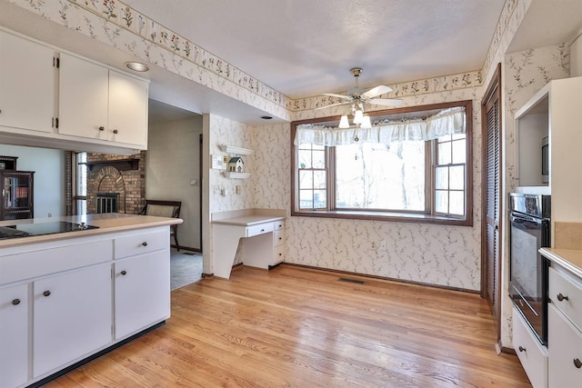 kitchen featuring light hardwood / wood-style flooring, ceiling fan, black appliances, white cabinets, and a brick fireplace