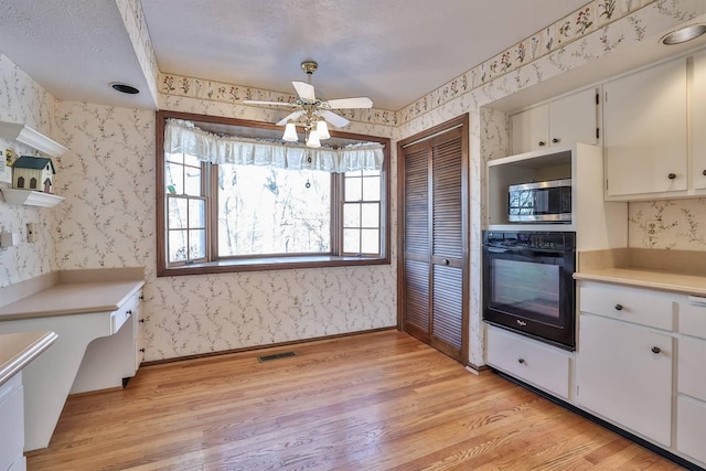 kitchen featuring stainless steel microwave, white cabinets, oven, ceiling fan, and light hardwood / wood-style floors