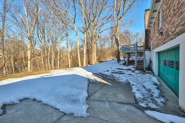 yard covered in snow featuring a wooden deck and a garage