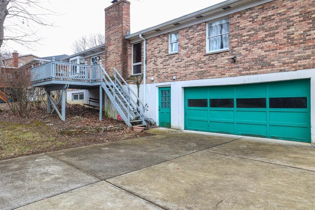 rear view of house with stairs, driveway, brick siding, and a chimney