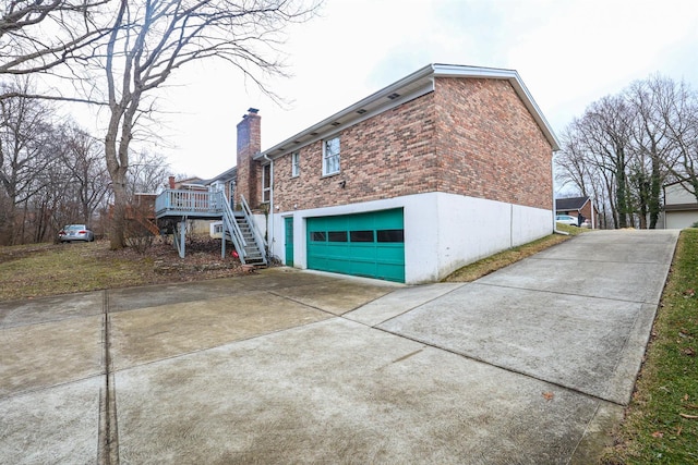 view of home's exterior with brick siding, a chimney, a garage, driveway, and stairs